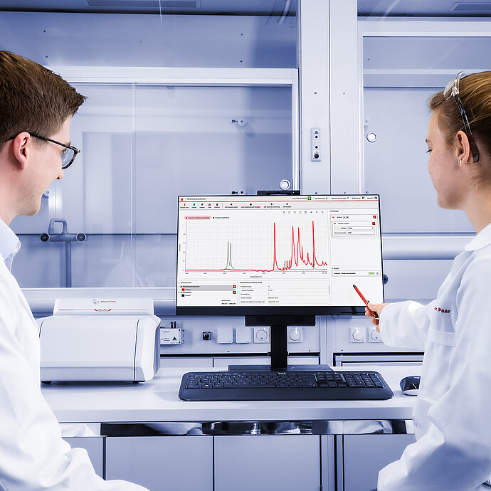 两名实验室技术人员正在操作一台放置在实验台上的 Lyza 3000 FTIR 光谱仪，前方中央的显示器上显示的是 Spectroscopy Suite 光谱分析软件